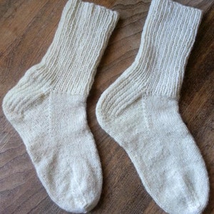 May include: Two pairs of white knitted socks. The socks are made of a soft, natural fiber and have a ribbed texture.