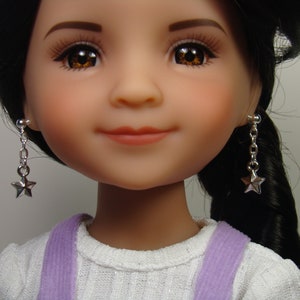 May include: A doll with long black hair wearing a white shirt with purple straps and silver star earrings.