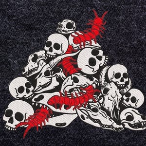 May include: Embroidered patch featuring a pile of white skulls and red centipedes on a dark gray background. The patch has a detailed design with black outlines and is suitable for jackets, bags, or other fabric items.