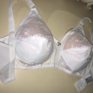 Könnte beinhalten: Weißer Spitzen-BH mit verstellbaren Trägern und einem Blumen-Detail. Der BH hat einen glatten, nahtlosen Cup und einen Haken- und Ösenverschluss.