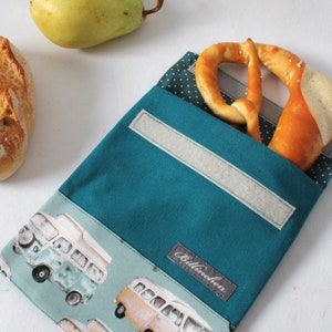 Könnte beinhalten: Tealfarbene Stoff-Lunch-Tasche mit weiß gepunktetem Futter. Die Tasche hat einen Klettverschluss und ein Etikett mit der Aufschrift "Billinchen". Die Tasche ist mit einem Muster aus Vintage-Volkswagen-Bussen verziert.