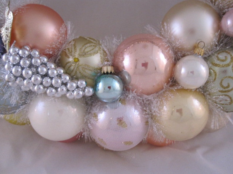 K&ouml;nnte beinhalten: Ein Weihnachtskranz, der mit wei&szlig;en, rosa und goldenen Kugeln und wei&szlig;em, flauschigem Besatz verziert ist.