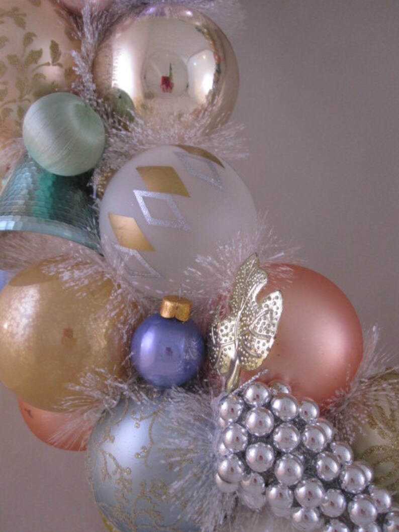 K&ouml;nnte beinhalten: Ein Weihnachtskranz, der mit verschiedenen Ornamenten geschm&uuml;ckt ist, darunter goldene, silberne und blaue Glaskugeln sowie wei&szlig;er, flauschiger Besatz. Der Kranz ist au&szlig;erdem mit einer Gruppe silberner Perlen verziert.