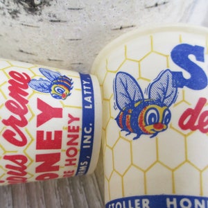 May include: Two vintage Stoller Honey cups. The cups are off-white with a honeycomb pattern and feature a cartoon bee illustration. Text includes "Stoller Honey" and "delicious honey".