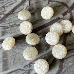 May include: A collection of 12 white iridescent round buttons with a speckled texture.