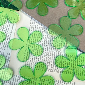 May include: Bright green, translucent acrylic flower shapes scattered on a vintage book page. These five-petal floral cutouts are ideal for crafting and scrapbooking projects.