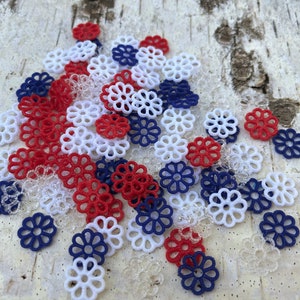 May include: A pile of red, white, and blue decorative paper flowers. The flowers are made of a delicate, lacy material and are perfect for adding a touch of whimsy to any craft project.
