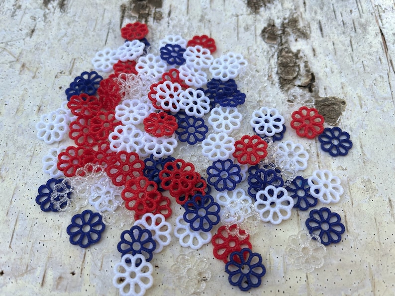 May include: A pile of red, white, and blue decorative paper flowers. The flowers are made of a delicate, lacy material and are perfect for adding a touch of whimsy to any craft project.