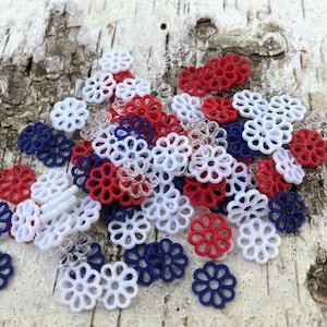 May include: A pile of red, white, and blue decorative plastic flowers. The flowers are all the same size and shape, and they are arranged in a random pattern.