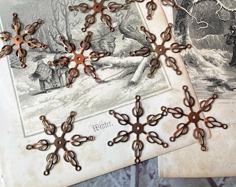 May include: A collection of six copper-colored metal snowflake-shaped findings, each featuring a central circular hole and six radiating arms with open, looped wire designs. These decorative components are arranged on a vintage paper background.