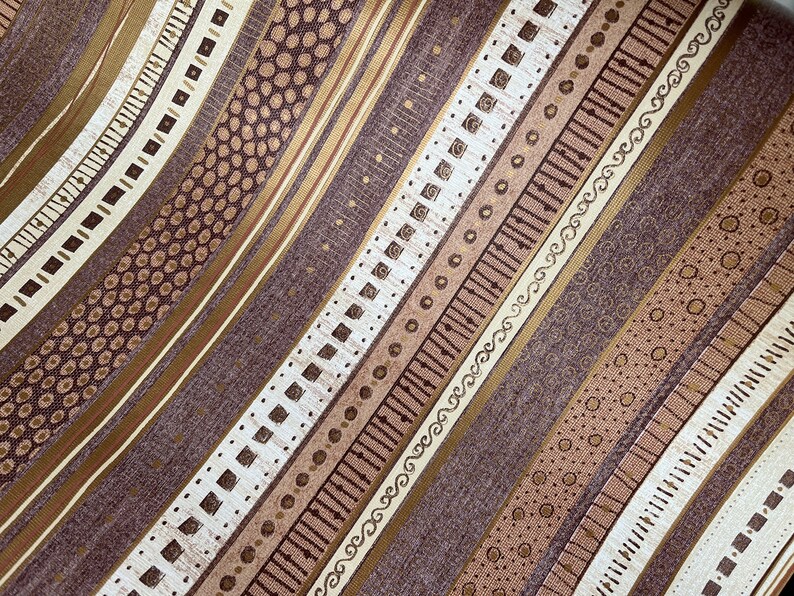 May include: A brown fabric with a repeating pattern of gold and white stripes. The stripes feature different geometric designs, including dots, squares, and swirls.