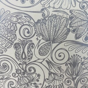 May include: A black and white patterned design featuring a peacock with a large, detailed tail, along with other floral and geometric shapes. The design is on a light brown background.