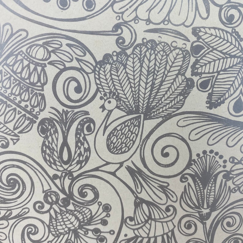 May include: A black and white patterned design featuring a peacock with a large, detailed tail, along with other floral and geometric shapes. The design is on a light brown background.