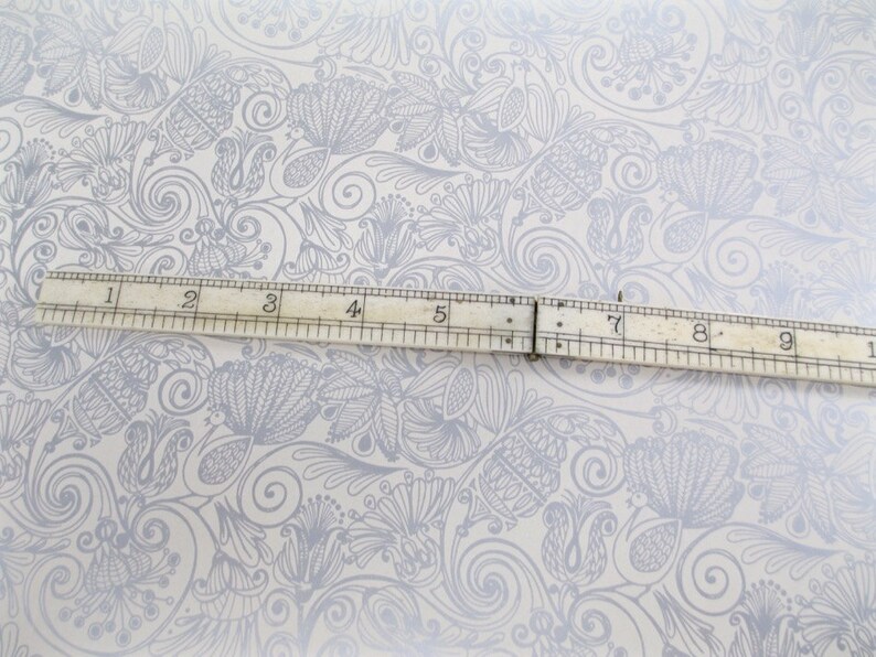 May include: A white background with a gray floral pattern. A ruler is placed horizontally across the center of the image. The ruler is marked with numbers from 1 to 10.
