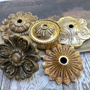 May include: A collection of five circular metal ceiling canopy plates featuring various embossed floral and geometric patterns in antique brass and gold finishes, each with a central hole for mounting hardware and wiring.