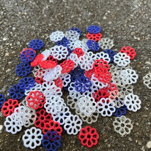 May include: A pile of red, white, and blue decorative flower-shaped embellishments. The embellishments are made of plastic and have a delicate, lacy design.