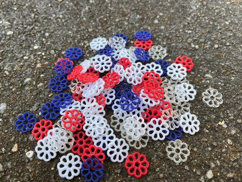 May include: A pile of red, white, and blue decorative flower-shaped embellishments. The embellishments are made of plastic and have a delicate, lacy design.