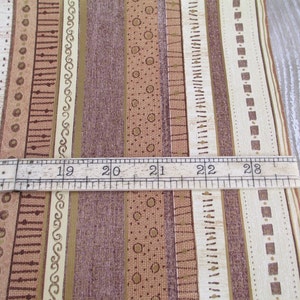May include: Close-up of a brown and beige striped fabric with a ruler measuring 17 to 23 inches. The fabric has a variety of patterns, including squares, circles, and lines.