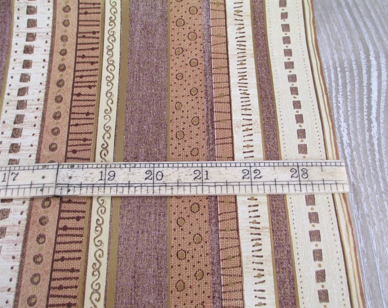May include: Close-up of a brown and beige striped fabric with a ruler measuring 17 to 23 inches. The fabric has a variety of patterns, including squares, circles, and lines.