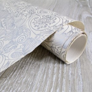 May include: A roll of white wallpaper with a gray floral pattern. The wallpaper is rolled up and the end of the roll is visible.