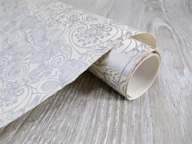 May include: A roll of white wallpaper with a gray floral pattern. The wallpaper is rolled up and the end of the roll is visible.
