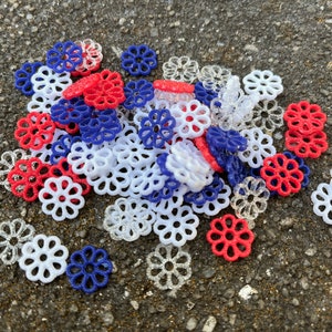 May include: A pile of red, white, and blue plastic flower-shaped embellishments. The embellishments are made of a delicate, lacy material.