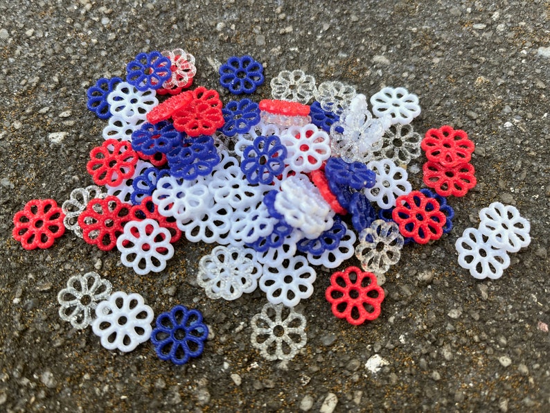 May include: A pile of red, white, and blue plastic flower-shaped embellishments. The embellishments are made of a delicate, lacy material.