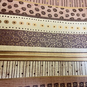 May include: A close-up of a patterned fabric with a repeating design of brown, gold, and white circles and lines. The fabric has a textured surface.