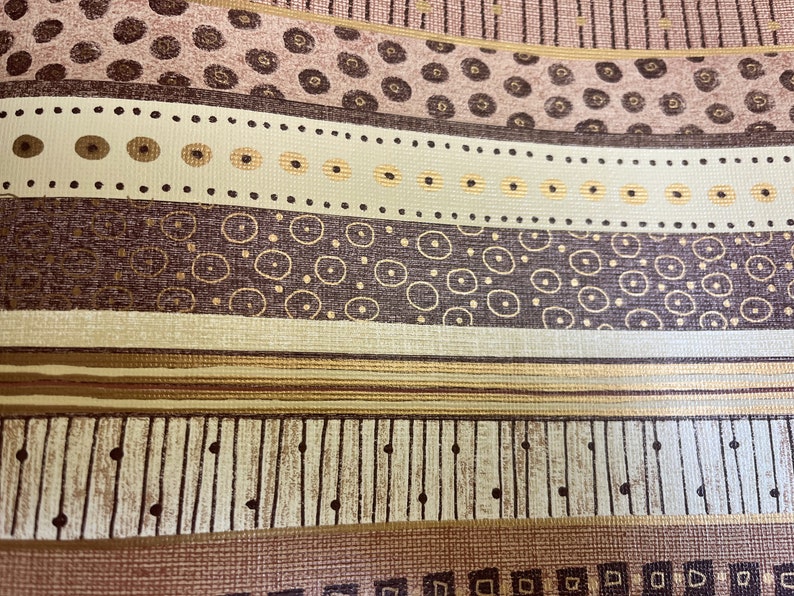 May include: A close-up of a patterned fabric with a repeating design of brown, gold, and white circles and lines. The fabric has a textured surface.