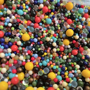 May include: A large collection of small, spherical beads in a wide variety of colors including yellow, red, blue, green, black, and white. The beads vary in size and finish, featuring opaque, translucent, and matte textures mixed together.