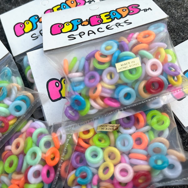 May include: A close-up of multiple bags filled with colorful plastic rings labeled "Pop Beads Spacers" and "Made in Hong Kong".
