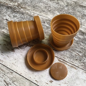 May include: A set of four brown plastic collapsible cups. The cups are nested inside each other and have a circular base. The cups are marked with numbers 1-6.