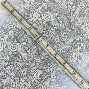 May include: A close-up of a white background with a silver-grey floral pattern. A ruler is placed diagonally across the image, with the numbers 3 through 11 visible.