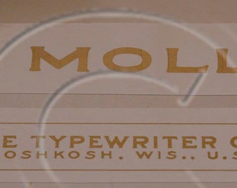 Può includere: Un'etichetta bianca con lettere dorate che recita "No. 3 Molle Typewriter Company, Oshkosh, Wis., U.S. of A."