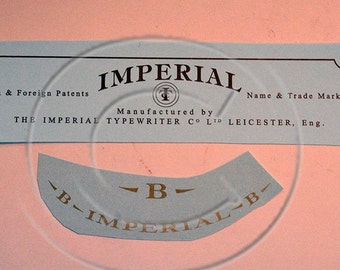 Può includere: Un'etichetta blu e bianca con il testo "IMPERIAL" in lettere nere. L'etichetta include anche il testo "British & Foreign Patents", "Manufactured by THE IMPERIAL TYPEWRITER CO LTD LEICESTER, Eng." e "Name & Trade Mark Regd".