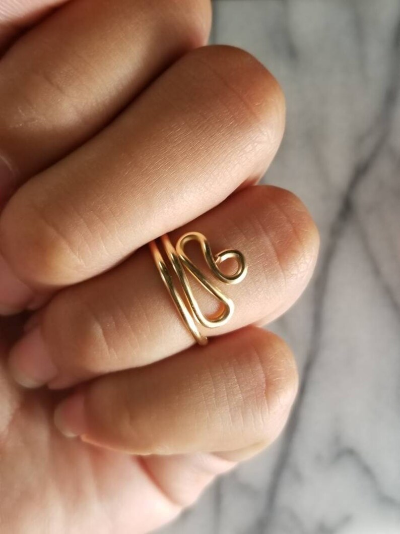 Pu&ograve; includere: Un anello in filo d'oro con un design astratto unico. L'anello &egrave; semplice e delicato, il che lo rende un'ottima scelta per l'uso quotidiano.
