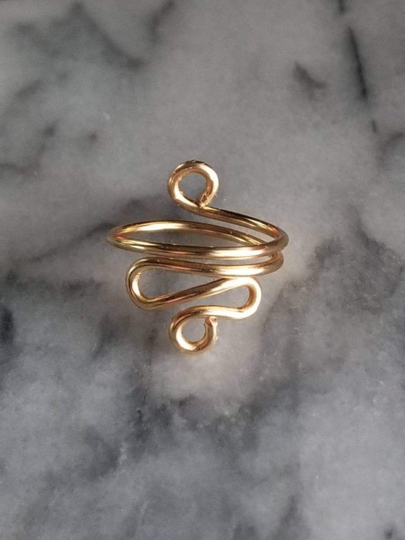 Pu&ograve; includere: Orecchino a cerchio in filo d'oro con un designo semplice e astratto. L'orecchino &egrave; realizzato con un unico filo di metallo attorcigliato e modellato a spirale.