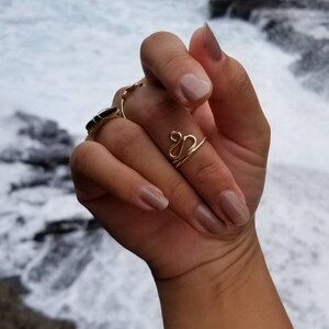 Pu&ograve; includere: Primo piano di una mano che indossa due anelli d'oro. L'anello sull'indice &egrave; una semplice fascia, mentre l'anello sul medio &egrave; un design a doppio anello. La mano &egrave; sullo sfondo di una spiaggia con onde che si infrangono.