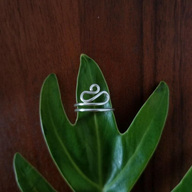 Pu&ograve; includere: Un anello d'argento con un design astratto unico. L'anello &egrave; realizzato in filo metallico e ha uno stile semplice e minimalista.