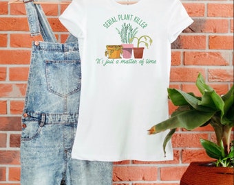 May include: White t-shirt with the text "SERIAL PLANT KILLER" above a graphic of three potted plants. Below the graphic is the text "It's just a matter of time." The shirt is hanging on a wooden hanger next to denim overalls.