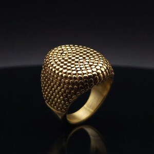 May include: A gold ring with a textured, dome-shaped top. The ring is made of metal and has a smooth band.
