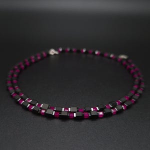 Può includere: Una collana a doppia fila con perline quadrate nere e perline color magenta. La collana è esposta su una superficie scura. La collana è progettata per essere indossata intorno al collo.