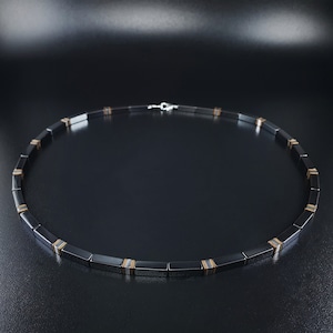 Peut inclure: Un collier noir avec des accents dorés. Le collier est composé de perles rectangulaires.