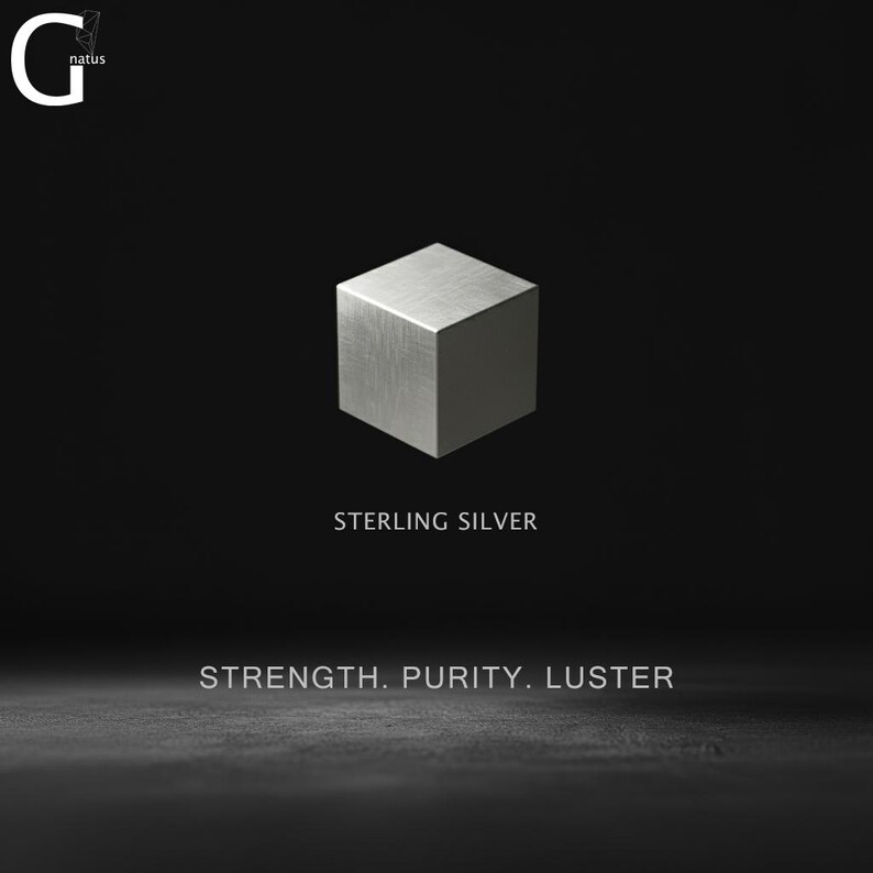 May include: A metallic silver cube centered against a black background. The text G natus appears in the top left corner. Below the cube, the text reads STERLING SILVER, followed by the words STRENGTH. PURITY. LUSTER in a clean, sans-serif font.