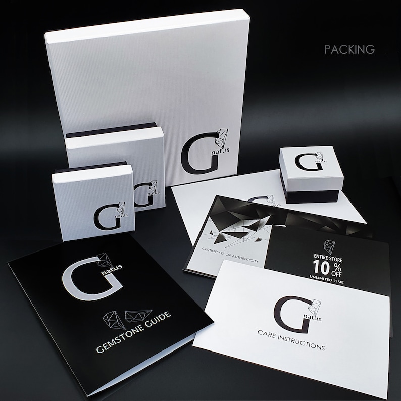 May include: A collection of white and black branded packaging boxes and printed cards featuring the G natus logo. The set includes a large square box, two smaller boxes, a Gemstone Guide, a Care Instructions card, and a Certificate of Authenticity.