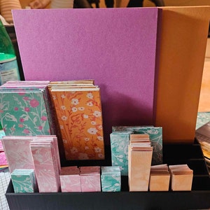 May include: A black organizer with a variety of colorful patterned paper cards. The cards are stacked in different heights and are arranged in a grid pattern. The organizer is made of wood and has a black finish.