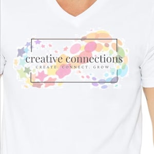 May include: White V-neck t-shirt with a colorful graphic design. The design features the text "creative connections" inside a black rectangle, surrounded by pastel-colored stars and circles. The text "CREATE. CONNECT. GROW." is below the main text.