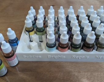May include: A white plastic storage case with 36 small bottles of ink. The bottles are organized into four categories: Subtles, Brights, Regals, and Neutrals.
