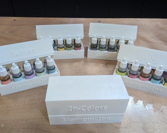May include: Five white plastic storage boxes with lids, each containing small bottles of ink. The boxes are labelled "Revals", "Neutrals", "Subtles", "Brights", and "In-Colors". Each box has the text "Stampin' Ink" on the front.
