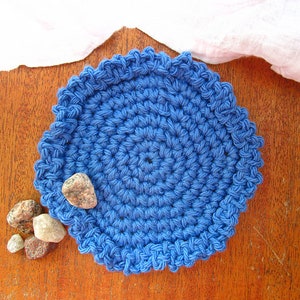 May include: A blue crocheted coaster with a scalloped edge. The coaster is on a wooden surface with small stones beside it.